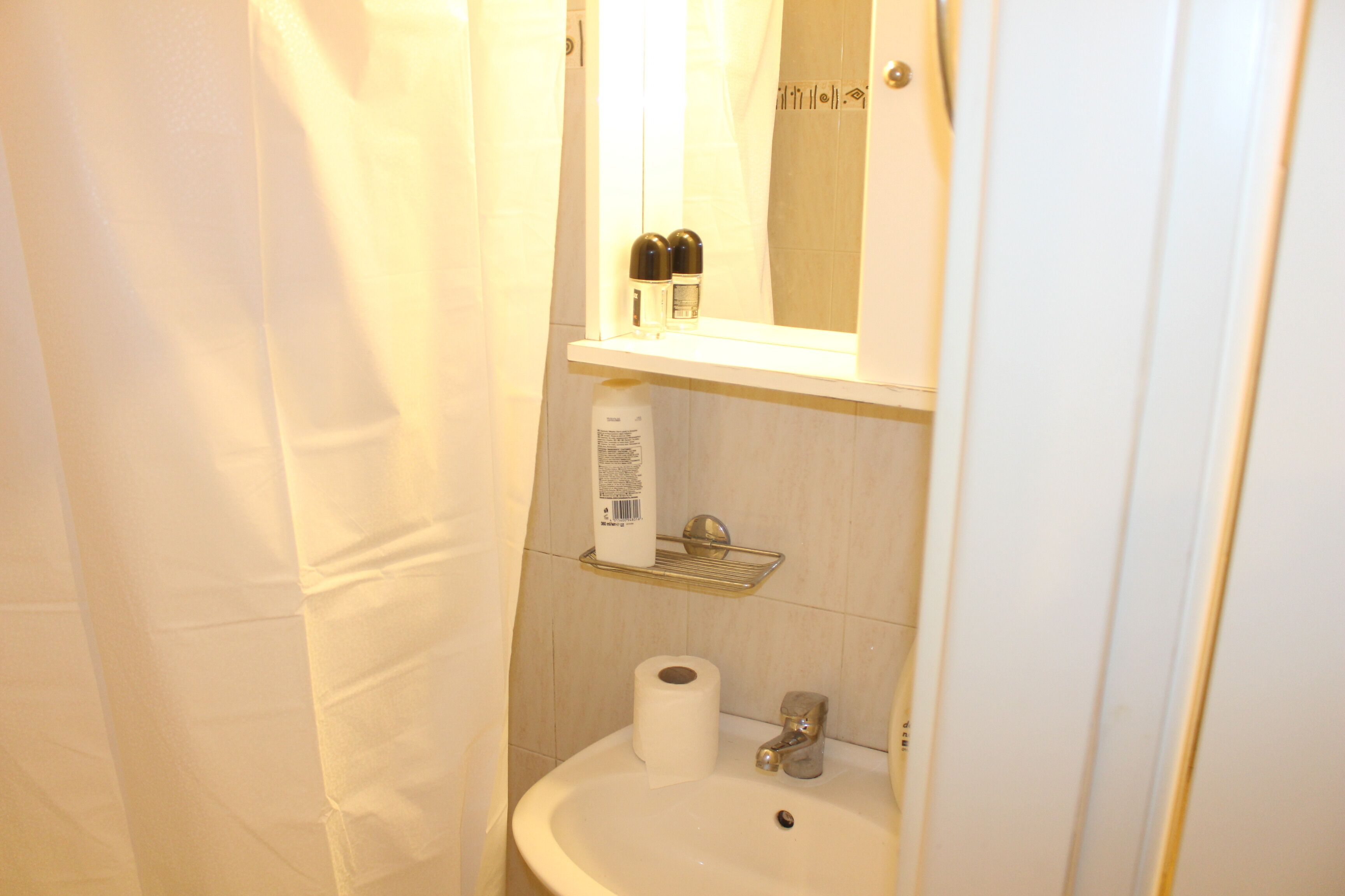 Un baño con lavamanos, espejo, cortina de ducha y estante con artículos de aseo.