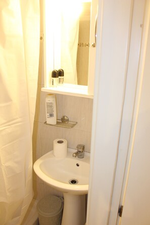 A bathroom with a sink, toilet paper, and a trash can. - 1-bedroom Apartment Center and City Attractions (Thessaloniki)
