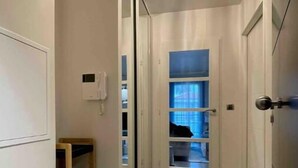 A hallway with a ceiling light fixture, a phone on the wall, and a door leading to a room with a blue window.