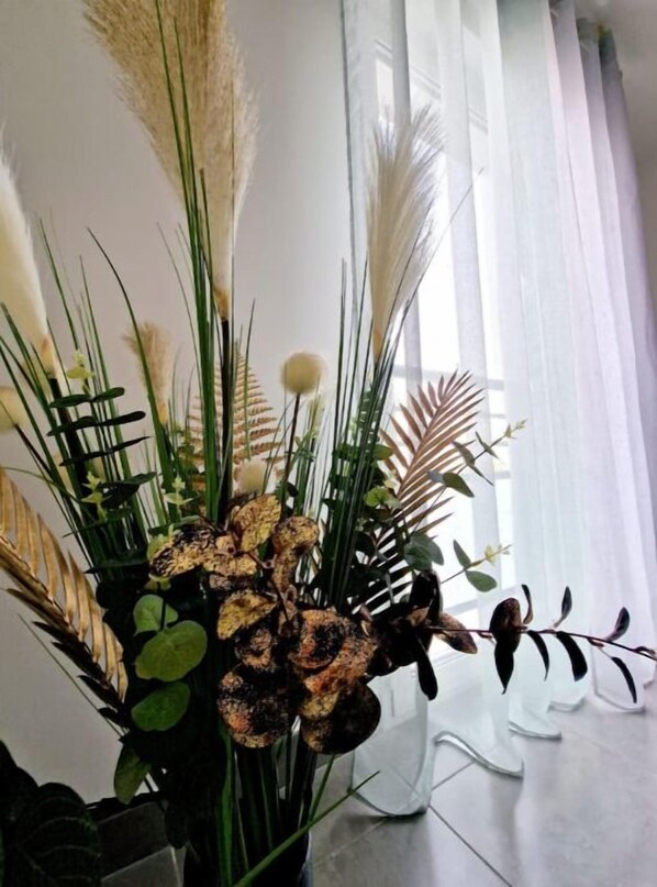 A room with a large window, a white chair, and a potted plant with various foliage.