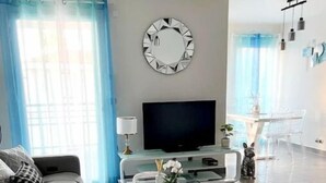 A modern living room with a sofa, a glass coffee table, a TV, and a round mirror on the wall.