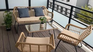 A balcony with wicker furniture, including a sofa and two chairs, a small table, and a potted plant.