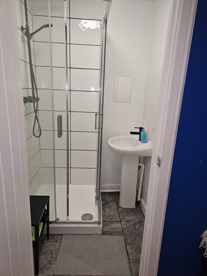 Kylpyhuoneessa on lasiseinällä varustettu suihku, valkoinen pesuallas ja sininen pullo työtasolla.