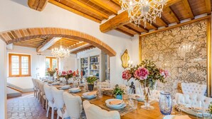 A dining area with a long wooden table set for a meal, surrounded by white upholstered chairs. - Fonte Di Pierdo - Eleven Bedroom Villa, Sleeps 22 (Castelfranco di sotto)