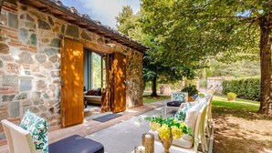 A stone building with a wooden door, a patio with outdoor furniture, and a garden with a tree. - Fonte Di Pierdo - Eleven Bedroom Villa, Sleeps 22 (Castelfranco di sotto)