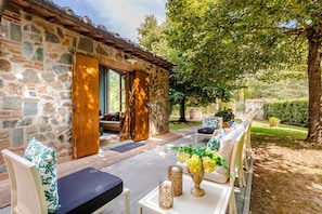 A stone building with a wooden door, a patio with outdoor furniture, and a garden with a tree. - Fonte Di Pierdo - Eleven Bedroom Villa, Sleeps 22 (Castelfranco di sotto)