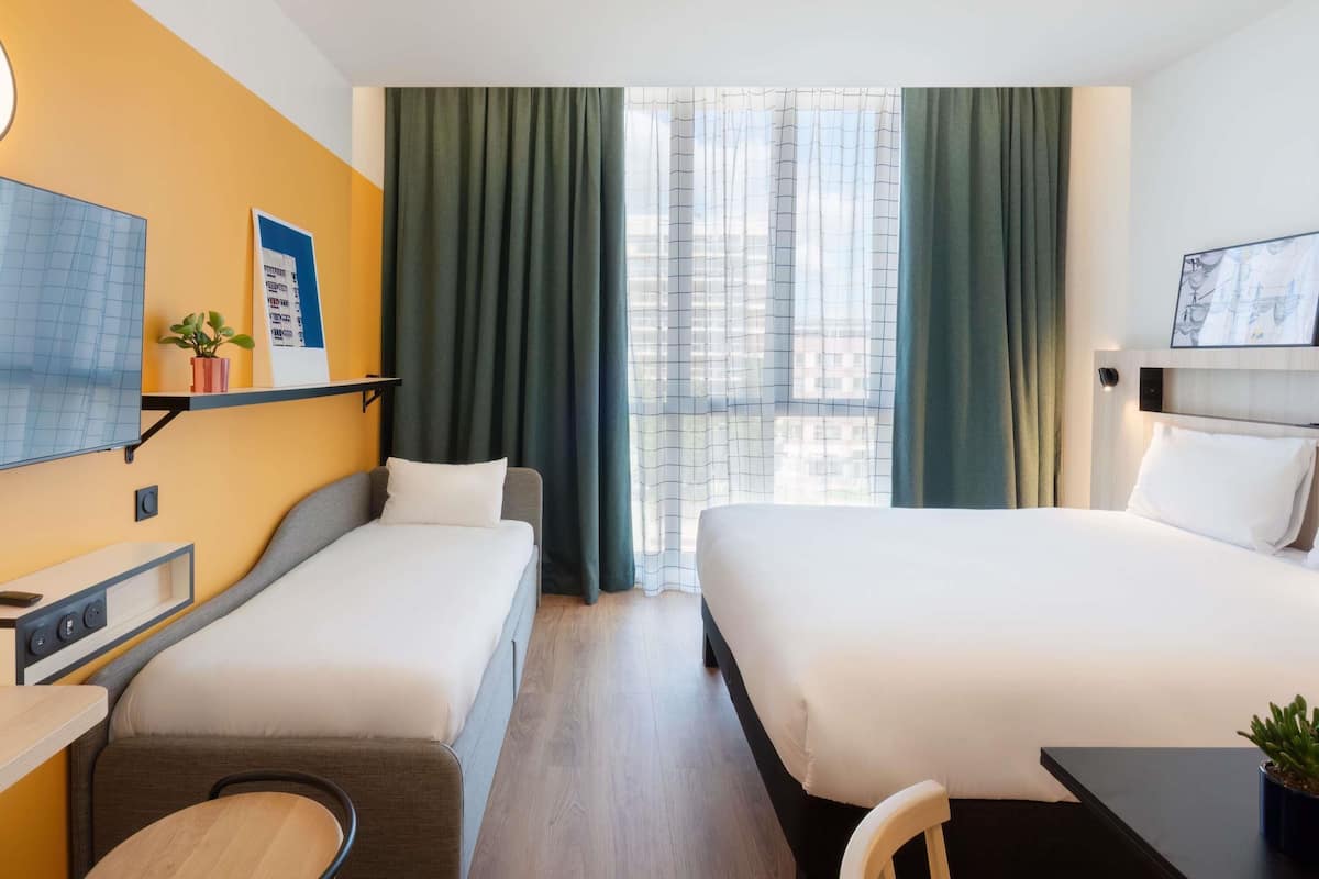 A hotel room with two beds, a desk, a TV, and a window with curtains.
