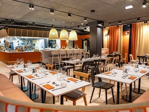 A restaurant with multiple tables set for dining, a kitchen area, and a bar. - Aparthotel Adagio Access Rouen Centre Cathédrale (Rouen)