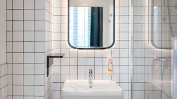 Un baño con paredes de azulejos blancos, un lavamanos blanco, un espejo, un perchero para toallas y una zona de ducha.