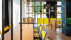 A modern interior with a wooden table and chairs, a bookshelf, and a large window with a view of greenery. - Aparthotel Adagio Access Rouen Centre Cathédrale (Rouen)