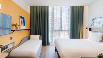Quarto de hotel com duas camas, uma escrivaninha, uma televisão e uma janela com cortinas.