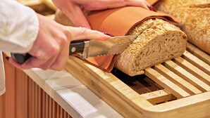A person cutting a loaf of bread on a wooden cutting board. - Aparthotel Adagio Access Rouen Centre Cathédrale (Rouen)