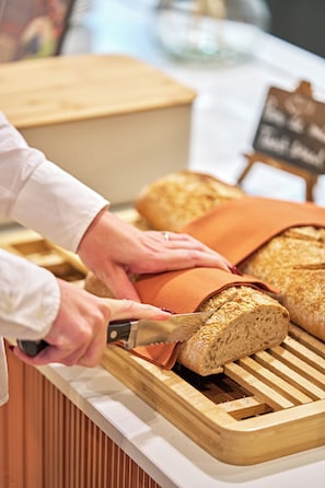 A person cutting a loaf of bread on a wooden cutting board. - Aparthotel Adagio Access Rouen Centre Cathédrale (Rouen)