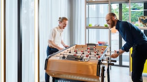 Two people playing foosball in a room with large windows and a view of greenery outside. - Aparthotel Adagio Access Rouen Centre Cathédrale (Rouen)