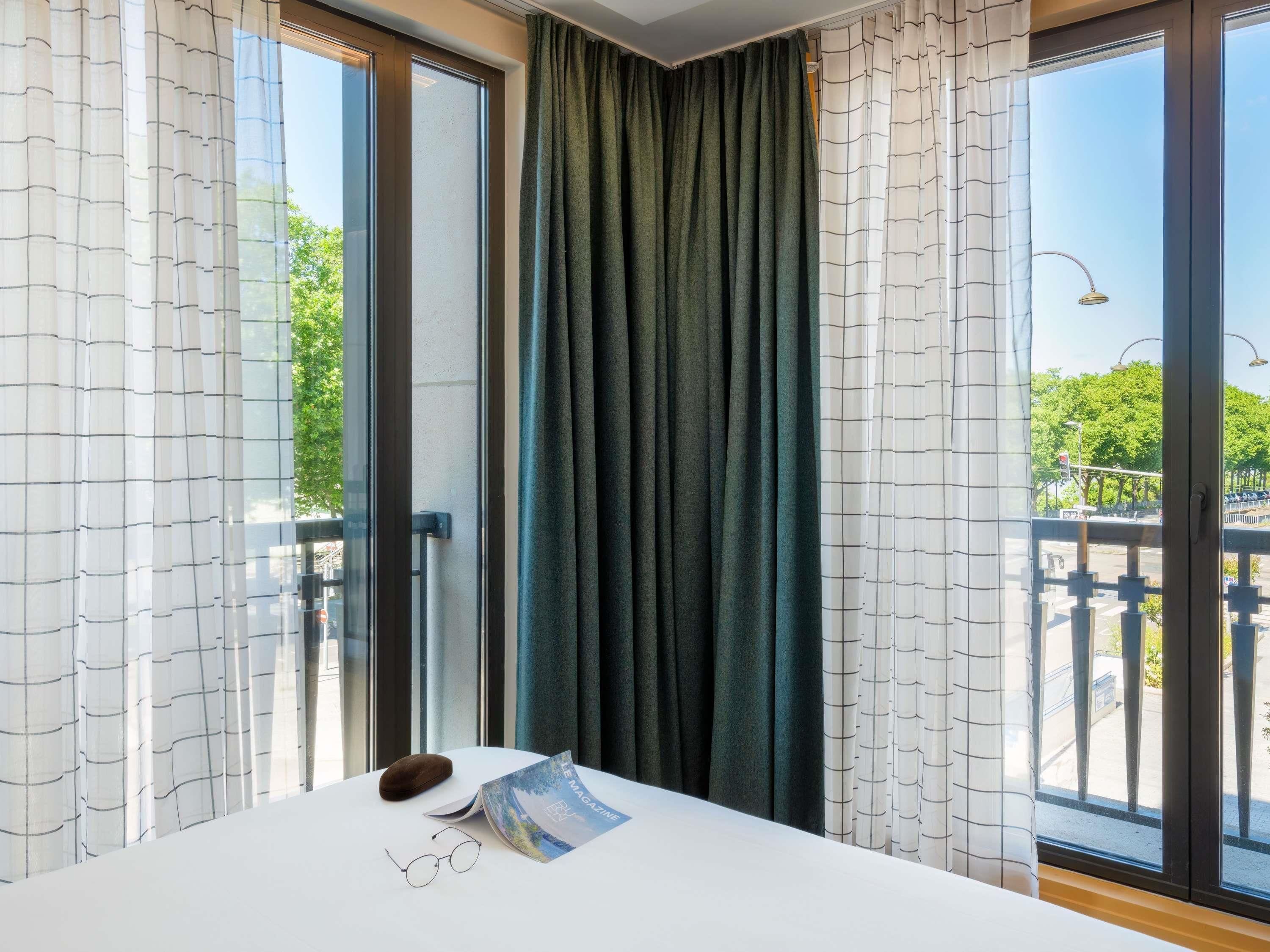 Une chambre d’hôtel avec un lit, une paire de lunettes, un magazine et un objet en bois posé sur la table de chevet.