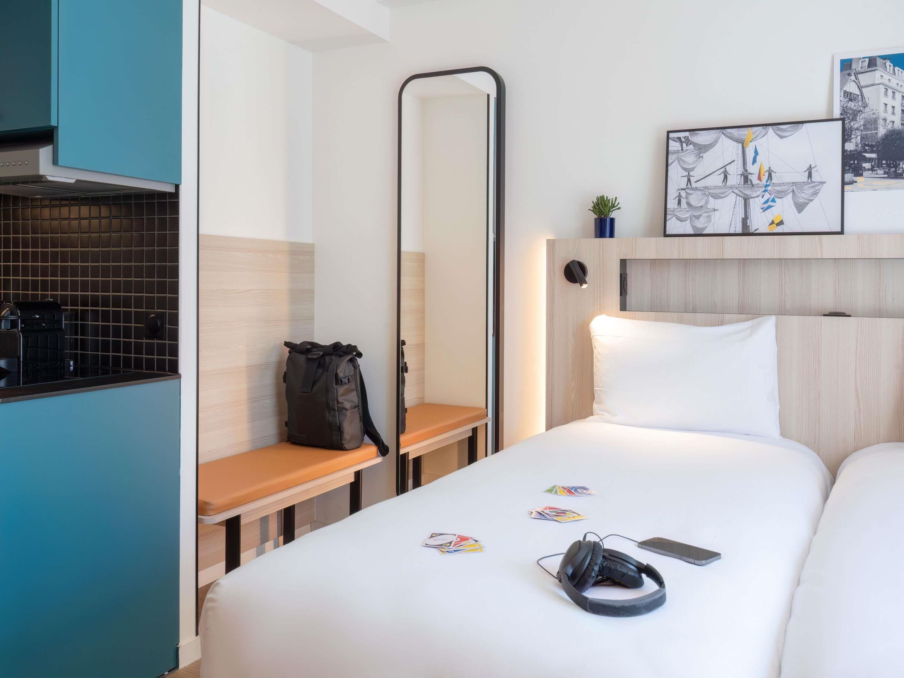 Habitación de hotel con cama, escritorio con una computadora portátil, espejo y un cuadro colgado en la pared.