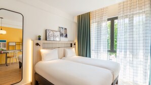 A hotel room with a large bed, a desk with a chair, and a view of greenery through the window. - Aparthotel Adagio Access Rouen Centre Cathédrale (Rouen)