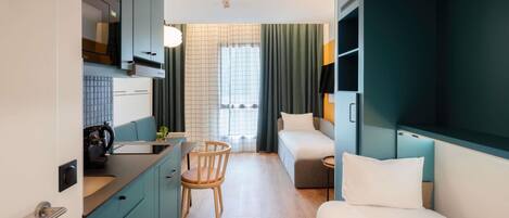 A compact hotel room with a kitchenette, a dining area, a bed, and a small table.