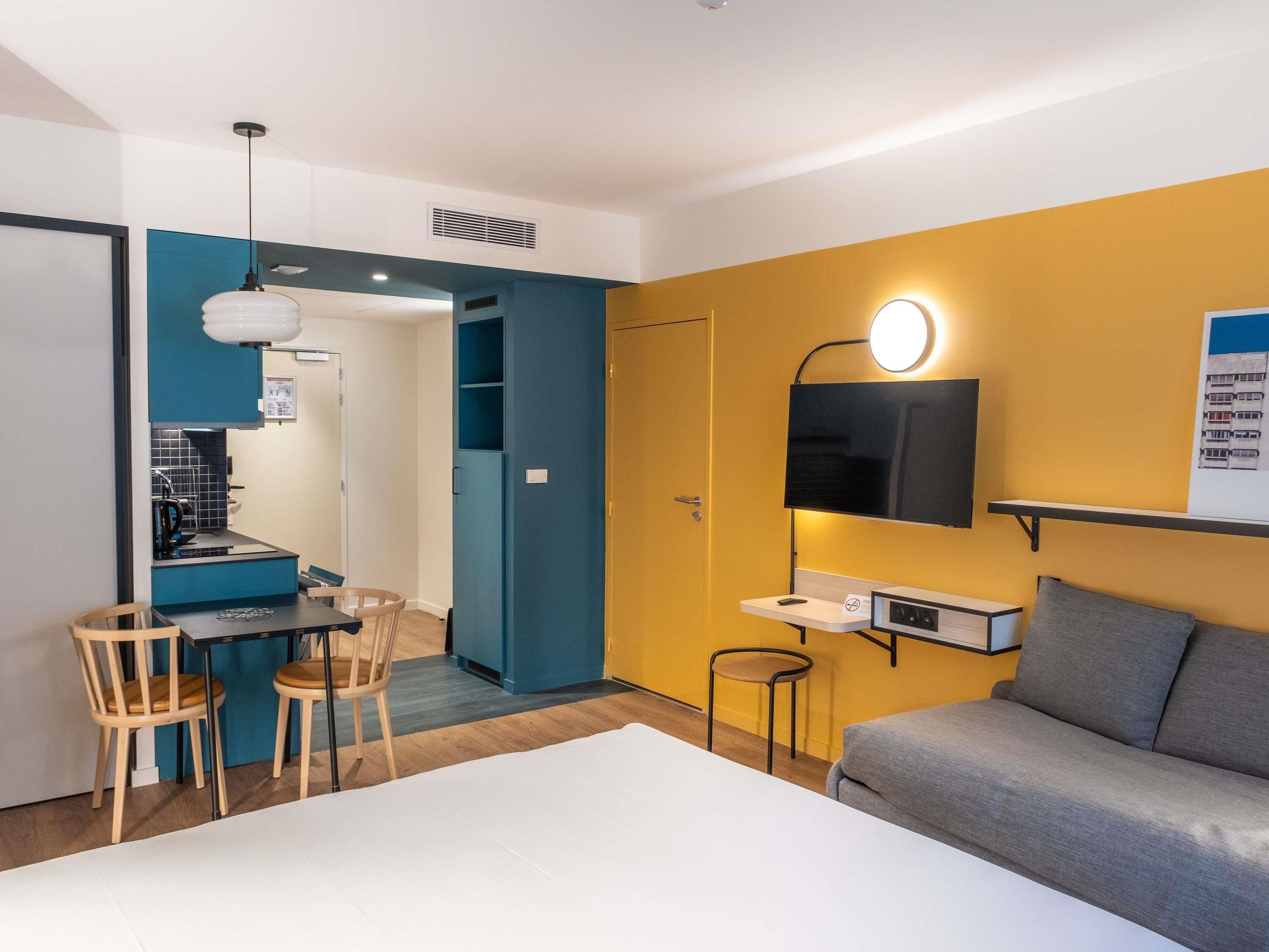Une chambre d’hôtel moderne dotée d’un coin repas, d’un canapé et d’un téléviseur fixé au mur.