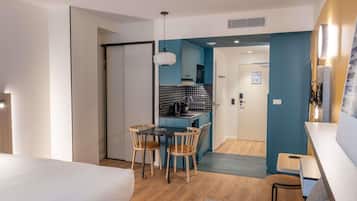 Quarto de hotel moderno com cama, área de refeições com cadeiras, uma pequena cozinha e banheiro.