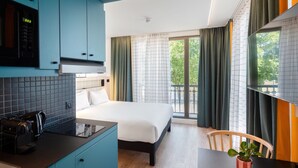 A modern hotel room with a bed, a small kitchenette, a dining area, and a balcony with curtains. - Aparthotel Adagio Access Rouen Centre Cathédrale (Rouen)