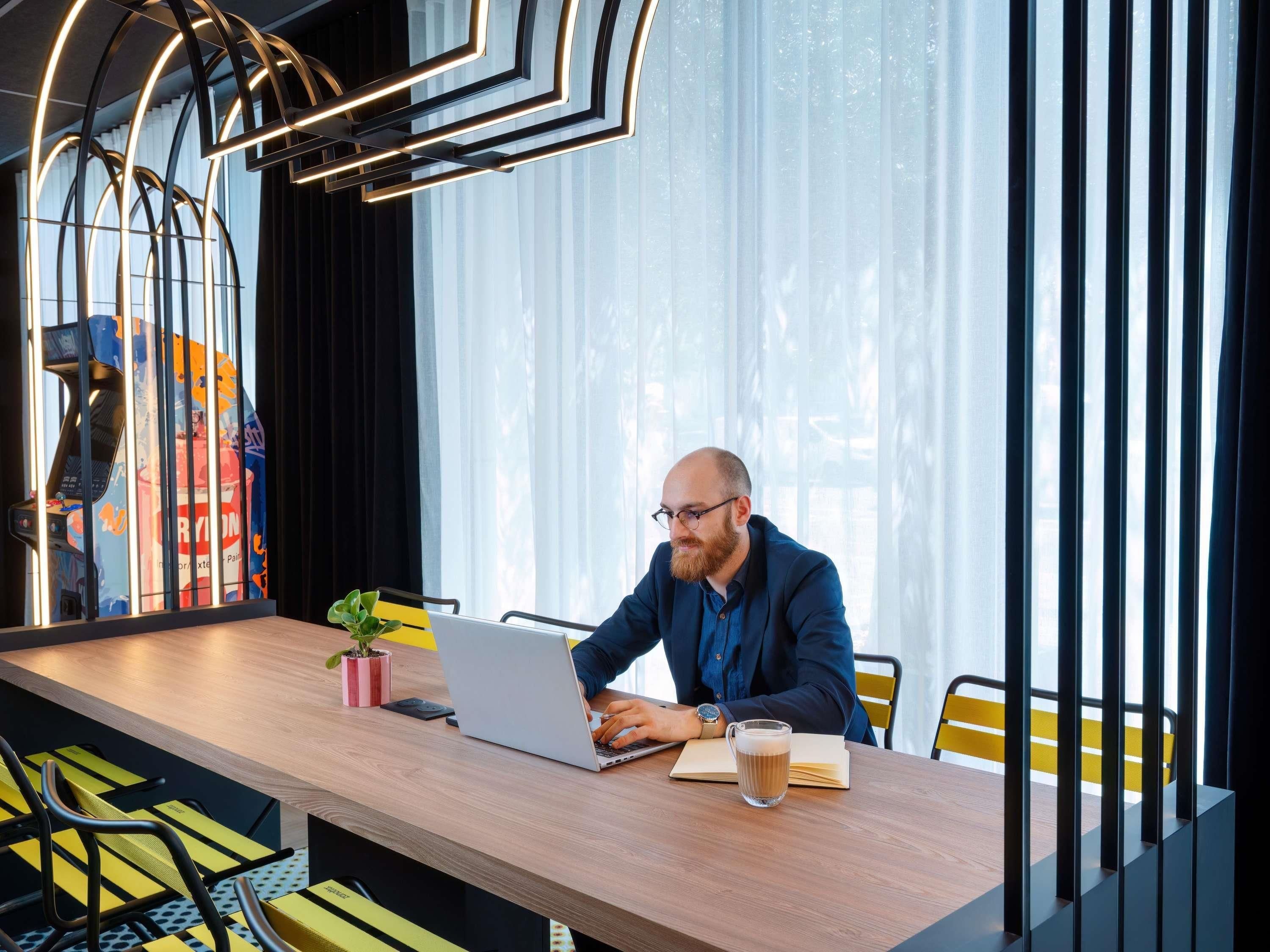 A person working at a wooden table with a laptop, a plant, and a coffee cup.