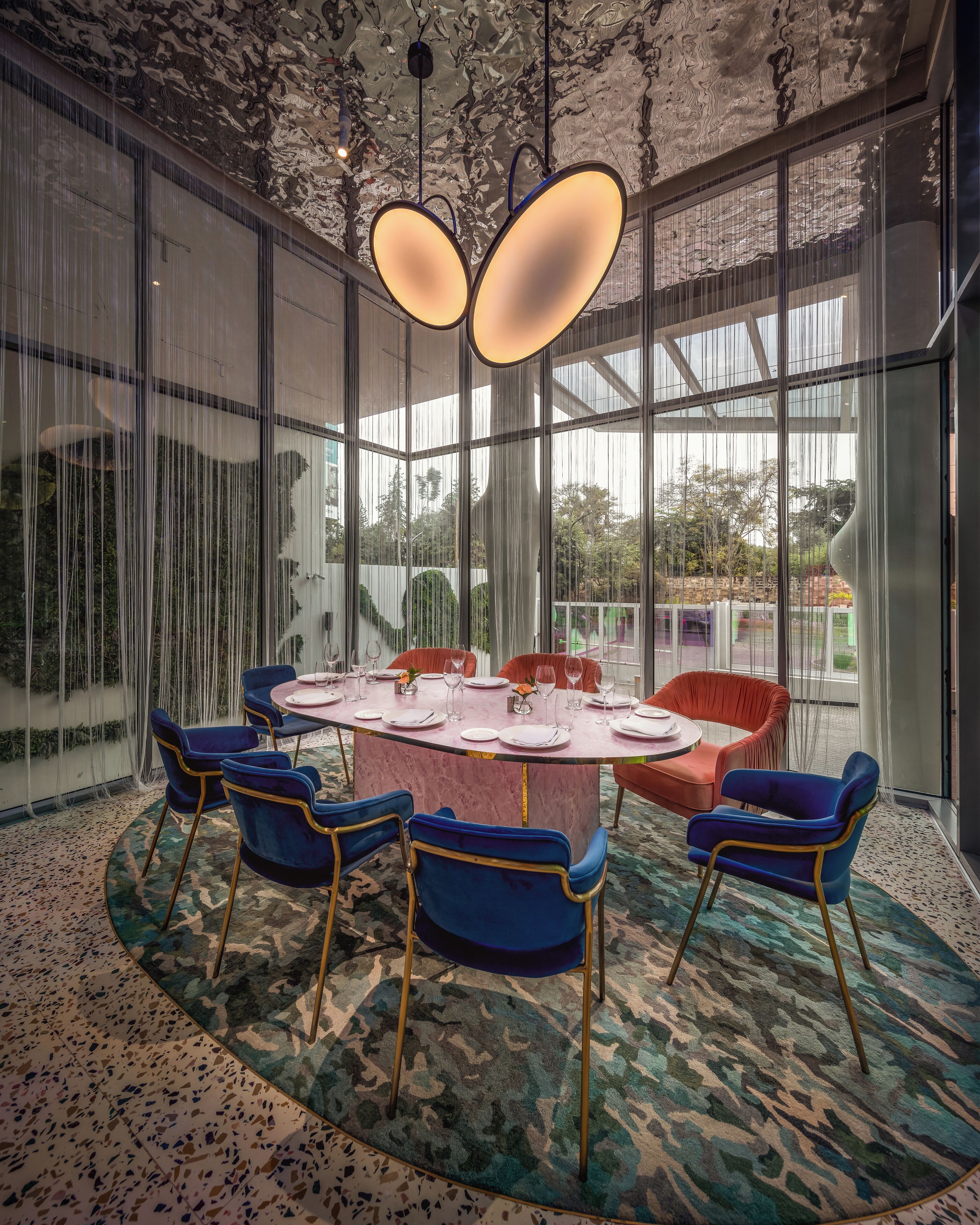 A modern dining area with a round table, blue chairs, and a patterned carpet.
