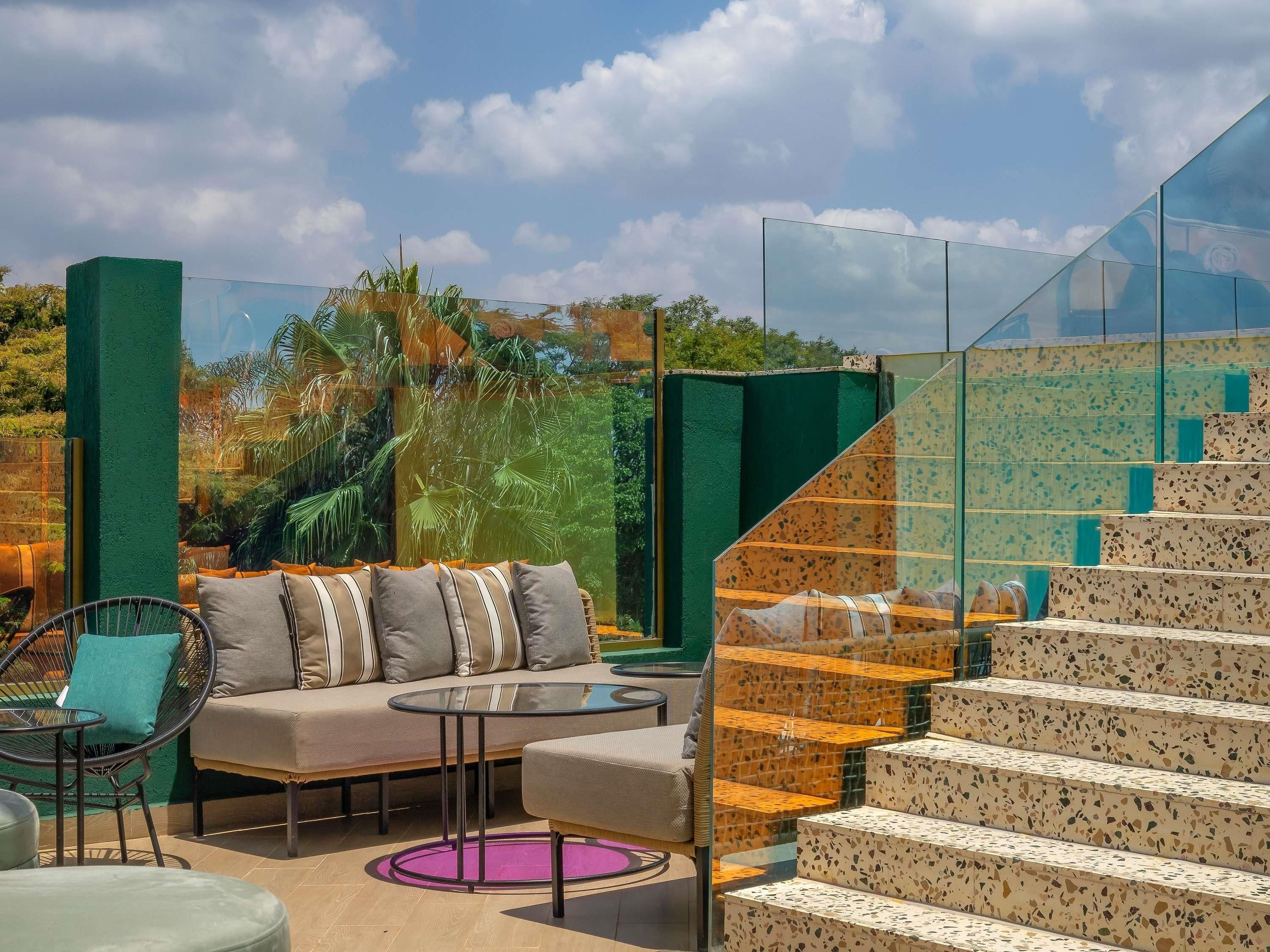 Un espacio exterior moderno con zona de estar, sofá, sillas y una mesa de vidrio.