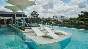A swimming pool with lounge chairs and umbrellas, a glass balustrade, and a view of a cityscape in the background.