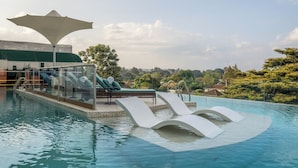 A swimming pool with a modern design, including a curved edge and a glass enclosure. There are lounge chairs and a shaded area with a canopy. - Gem Forest Hotel Nairobi - MGallery Collection (Nairobi)