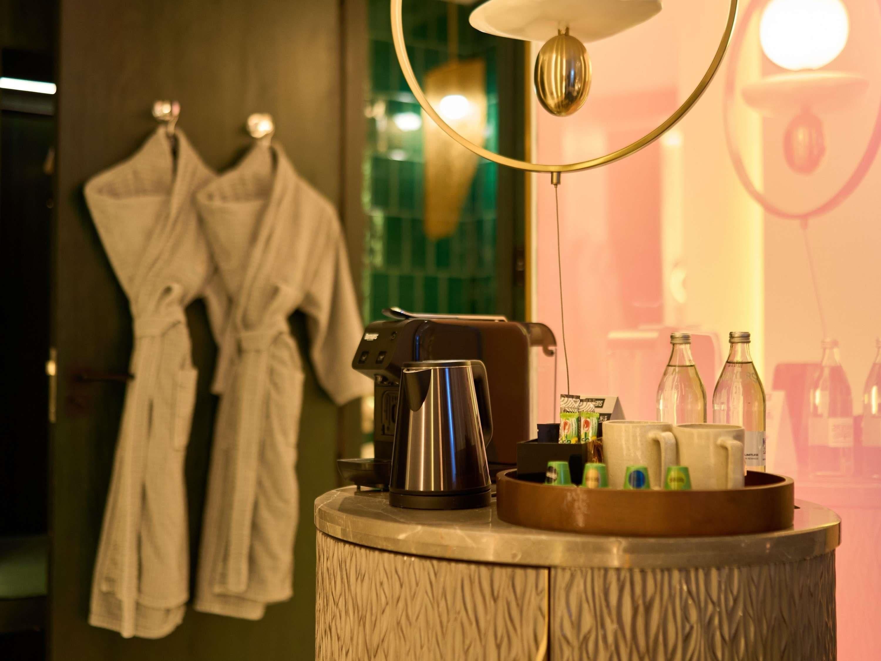 Ein Badezimmer mit Handtuchhalter, der zwei weiße Bademäntel, eine Kaffeemaschine und ein Tablett mit Toilettenartikeln zeigt.