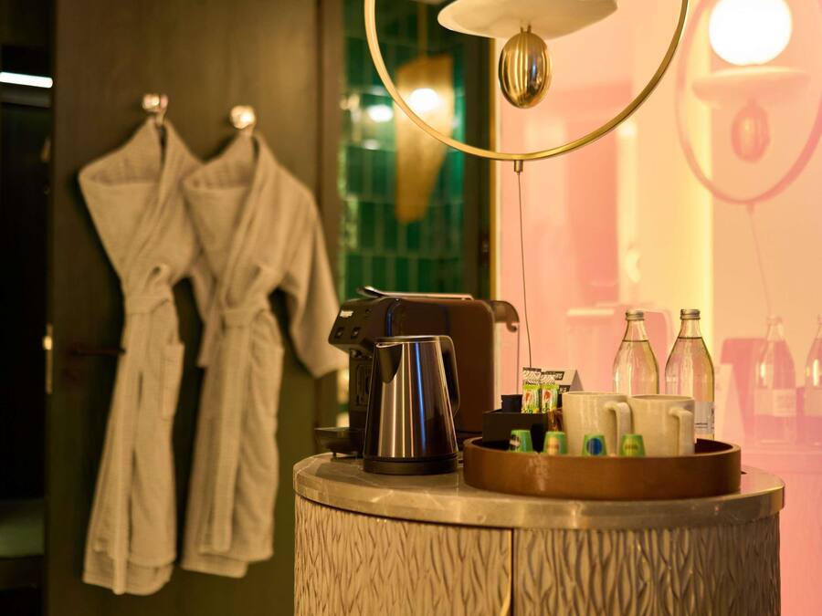 Ein Badezimmer mit Handtuchhalter, der zwei weiße Bademäntel, eine Kaffeemaschine und ein Tablett mit Toilettenartikeln zeigt.