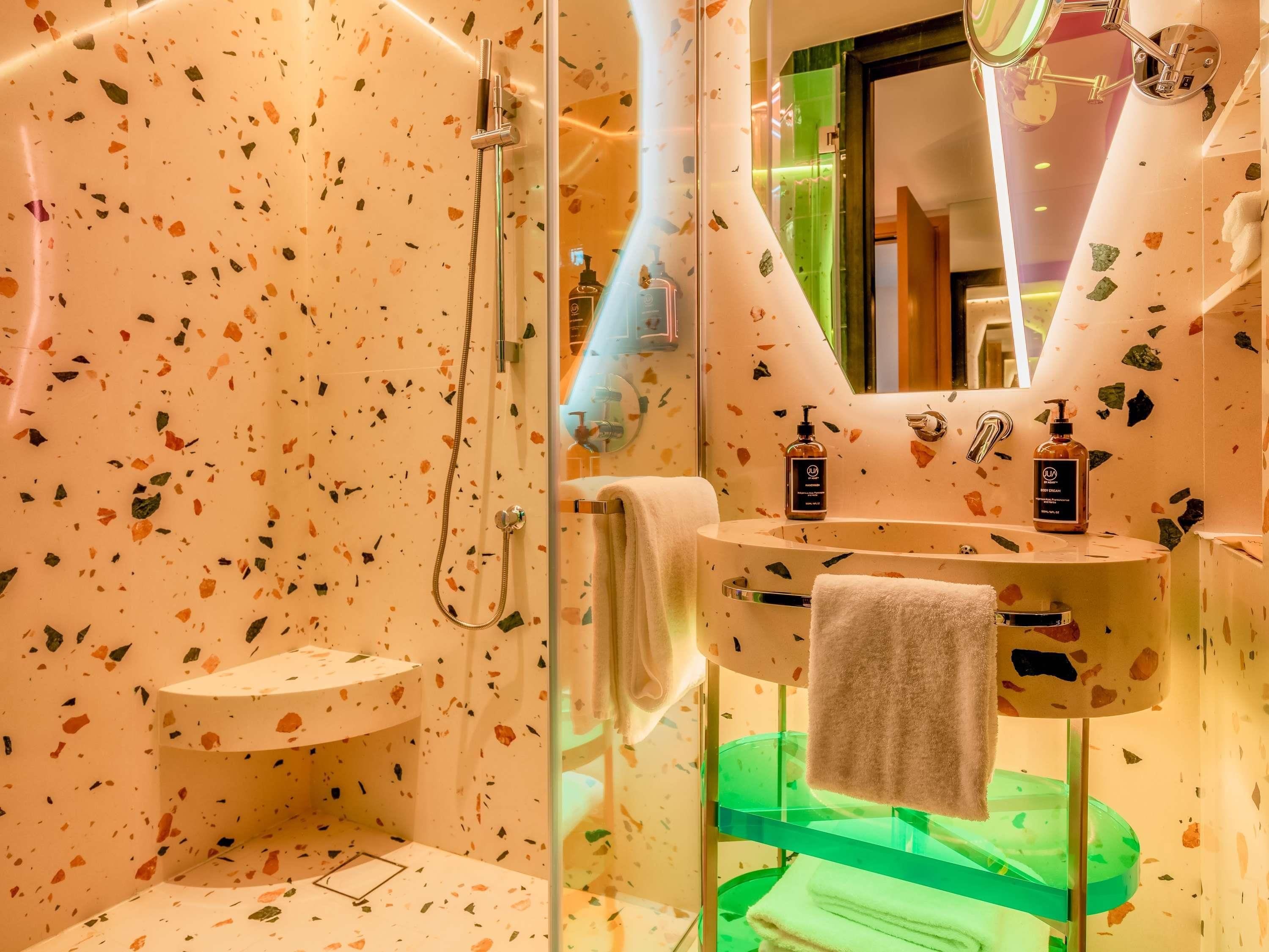 A bathroom with a shower, a sink with a mirror, and a green shelf.