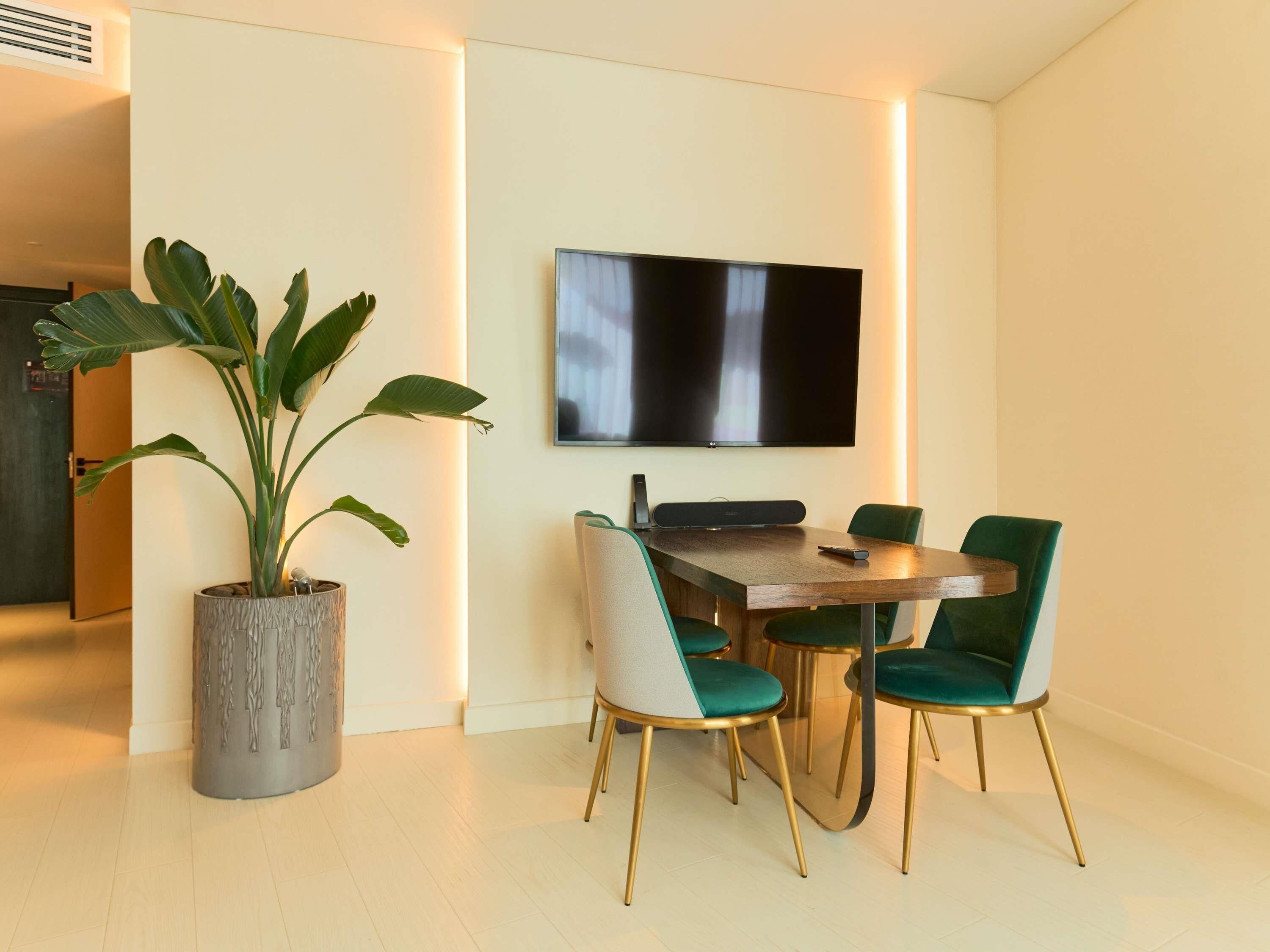 Un comedor con mesa, sillas, una planta en maceta y un televisor de pantalla plana montado en la pared.