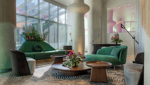 A modern lobby with green sofas, round coffee tables, and a large pillar. - Gem Forest Hotel Nairobi - MGallery Collection (Nairobi)
