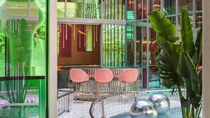 A modern interior with glass walls, a seating area with pink chairs, and a water feature. - Gem Forest Hotel Nairobi - MGallery Collection (Nairobi)