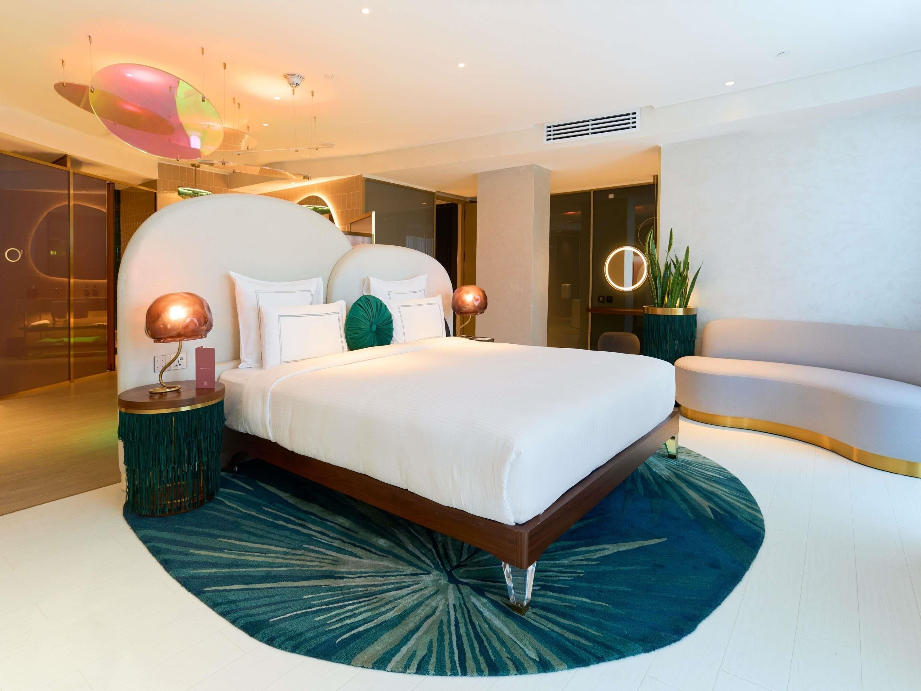 Une chambre moderne avec un grand lit, deux lampes de chevet, un miroir rond et une plante en pot.