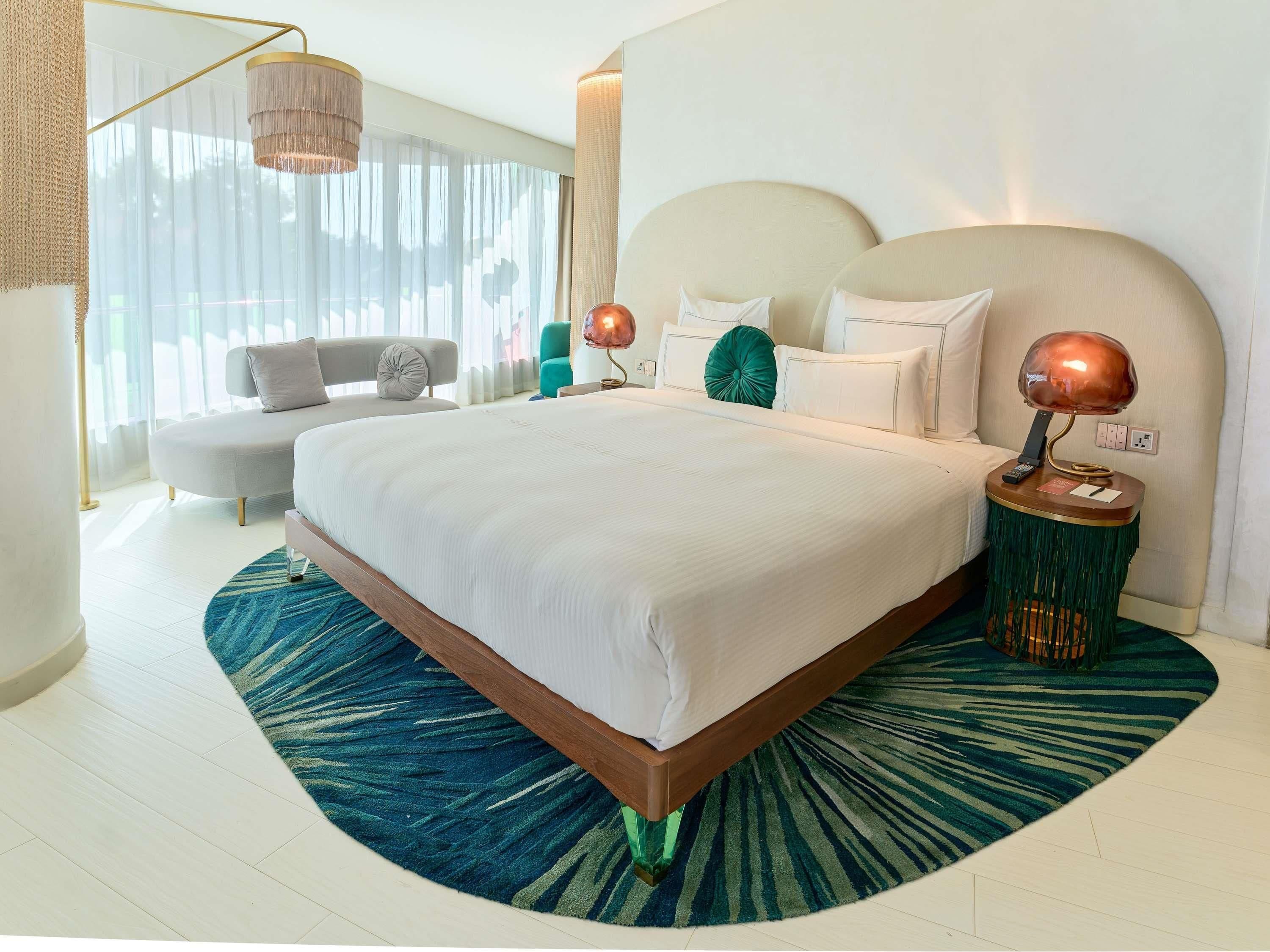 A modern bedroom with a large bed, bedside lamps, and a view of the outdoors through sheer curtains.