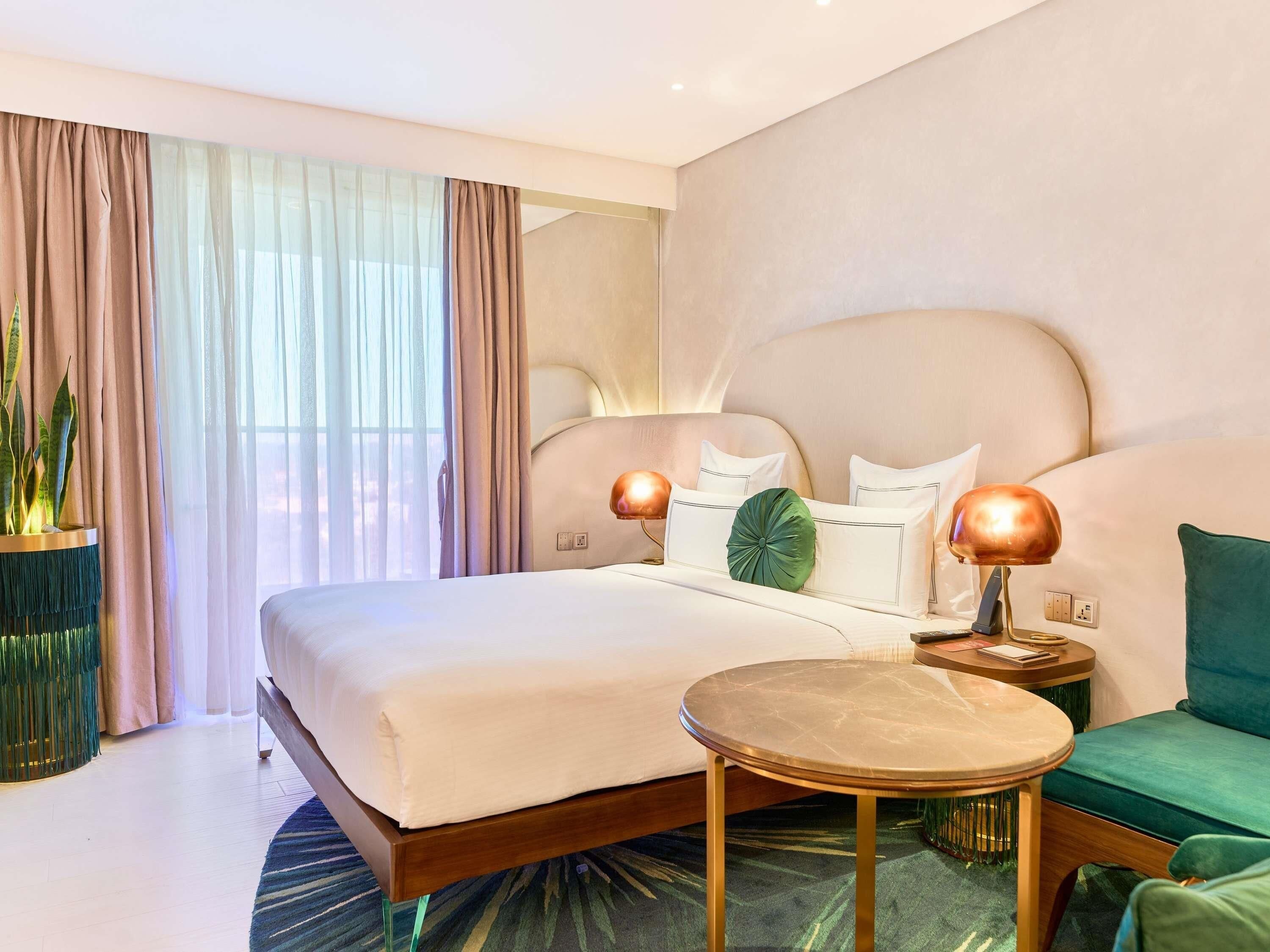 Une chambre d’hôtel avec un grand lit, des lampes de chevet, une table ronde, un canapé vert et une plante en pot.
