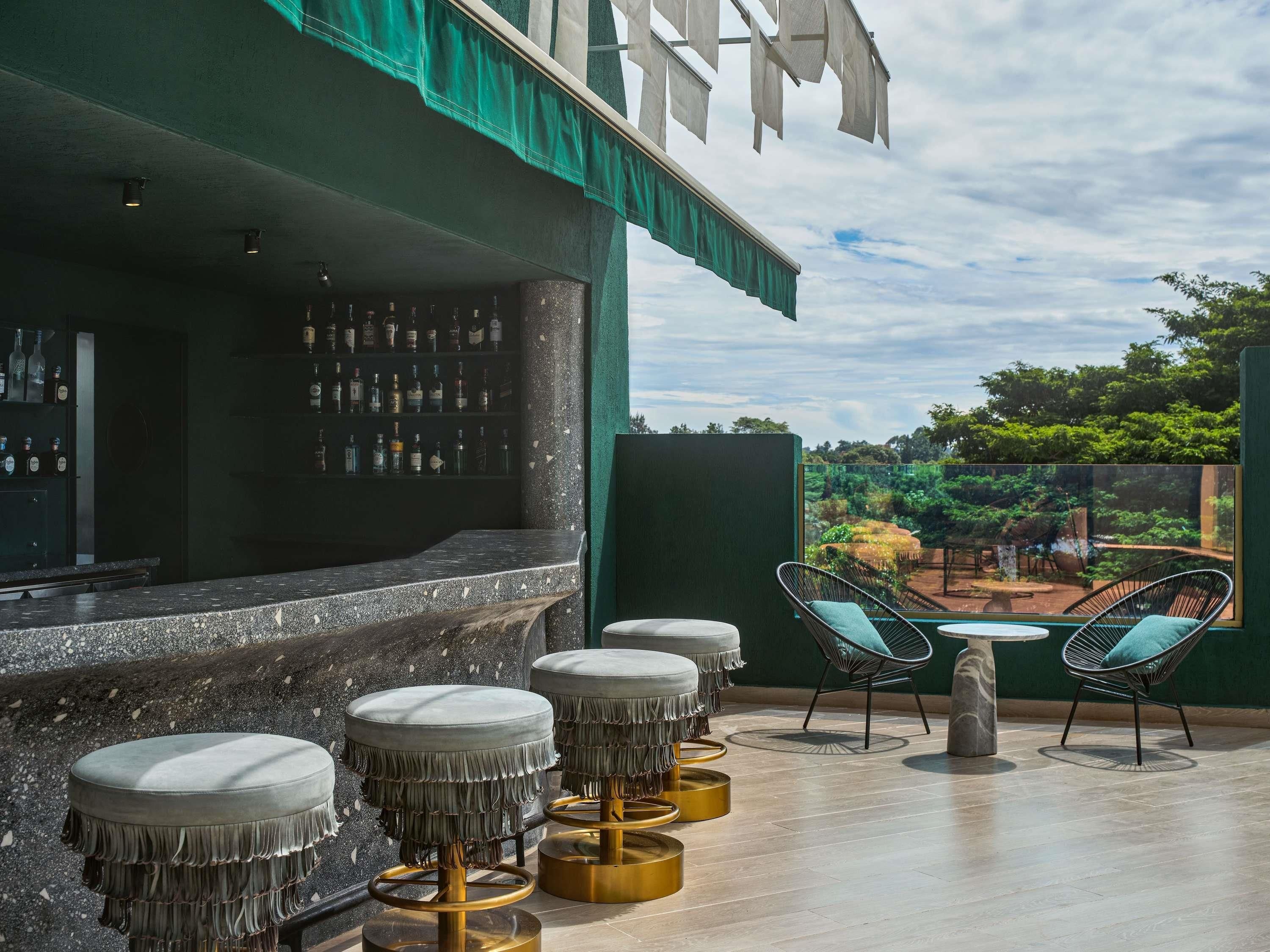 A bar area with a counter, stools, and chairs, with a view of greenery outside.