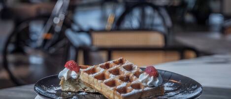 A waffle with whipped cream and a strawberry on a plate, placed on a marble table in a restaurant setting.