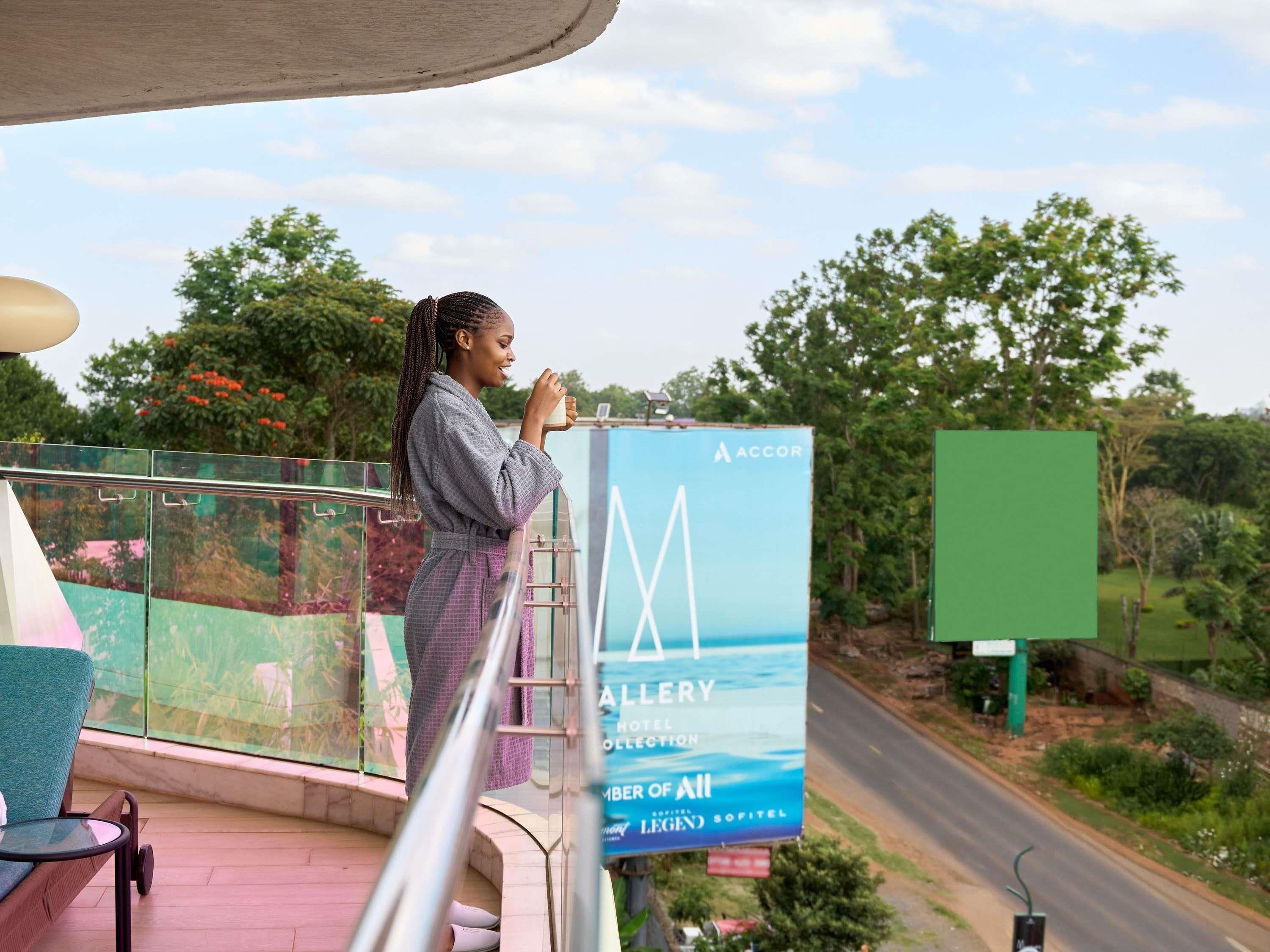 A person standing on a balcony with a view of a road and greenery.