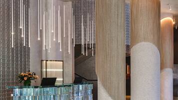 Un lobby moderno con mostrador de recepción de cristal, lámparas colgantes y amplias columnas.