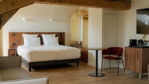 A modern hotel room with a wooden ceiling, a large bed with white linens, a desk with a chair, a television, and a minibar. - Hotel Fort St Laurent Lyon - Handwritten Collection (Lyon)
