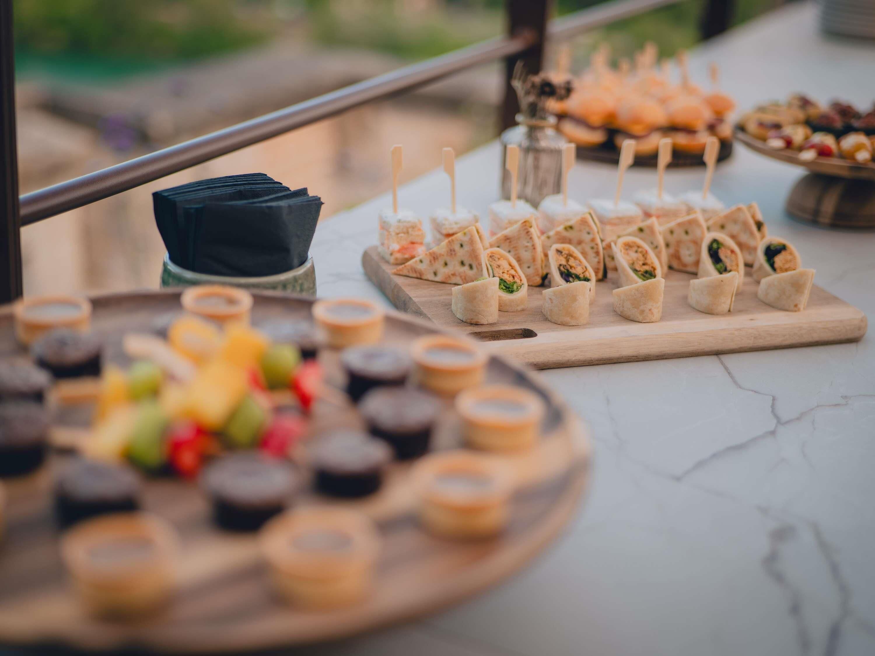 Una mesa de bufé con diferentes opciones de comida, incluyendo wraps y aperitivos, dispuestas sobre tablas de madera y un plato redondo.