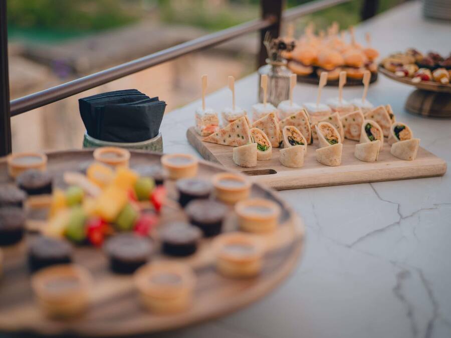 Una mesa de bufé con diferentes opciones de comida, incluyendo wraps y aperitivos, dispuestas sobre tablas de madera y un plato redondo.