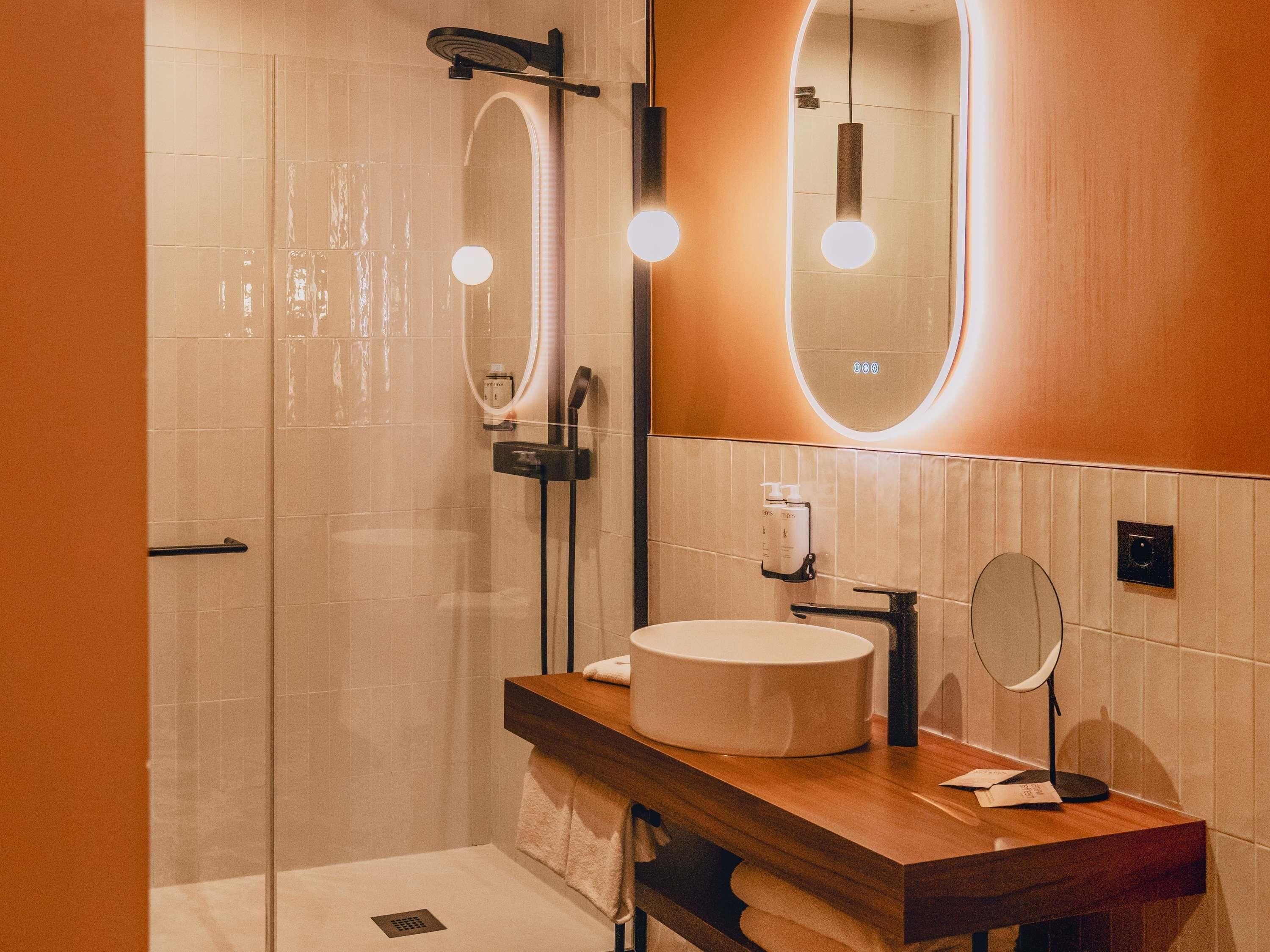 A modern bathroom with a glass-enclosed shower, a round mirror, and a wooden vanity with a sink.