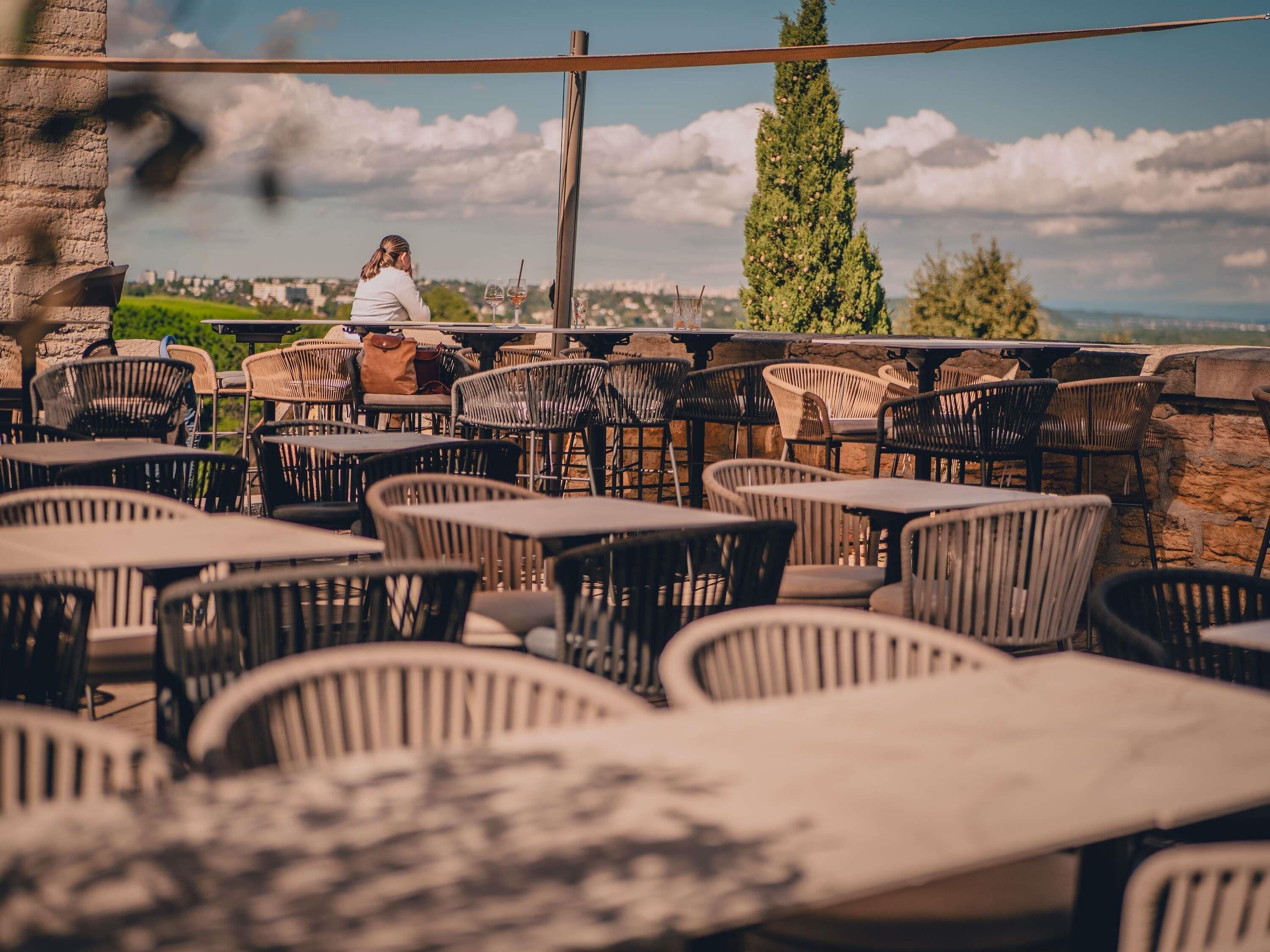 Un espace extérieur aménagé avec des chaises et des tables en osier, offrant une vue sur le paysage urbain.