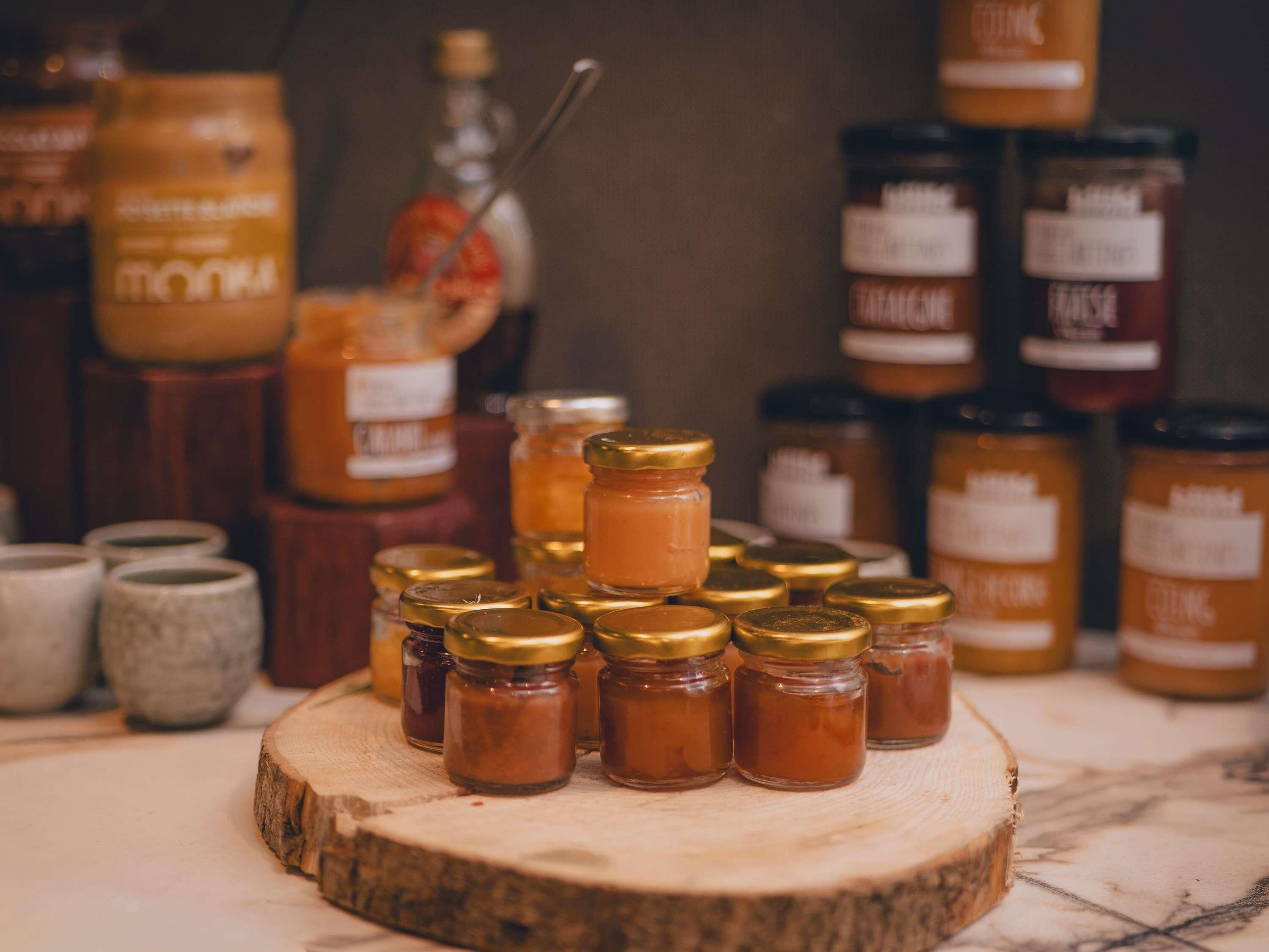 Variedad de frascos con tapas doradas sobre una superficie de madera, probablemente conteniendo conservas o salsas.