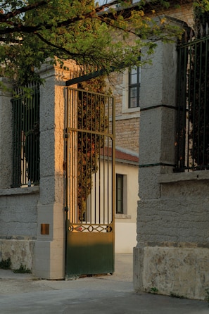 A gated entrance with a metal gate, a stone wall, and a building with a tiled roof. - Hotel Fort St Laurent Lyon - Handwritten Collection (Lyon)